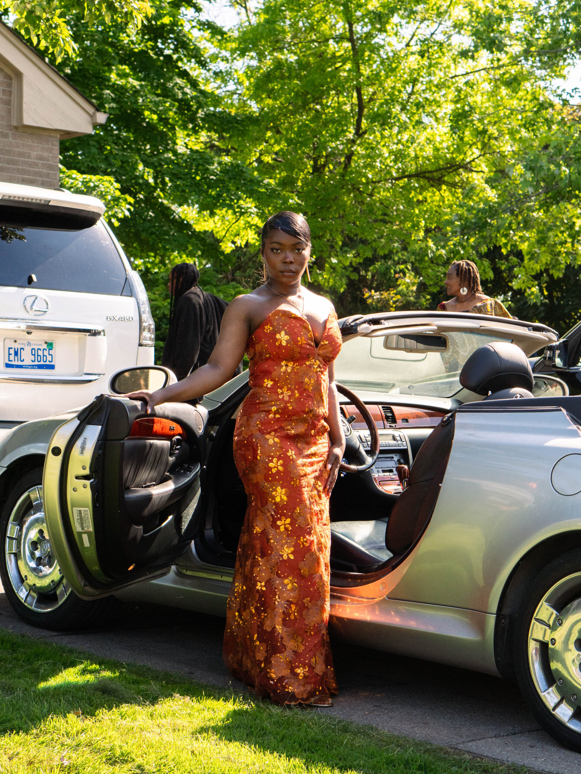 Angel Aharauka posing by her Lexus convertible car in a prom dress